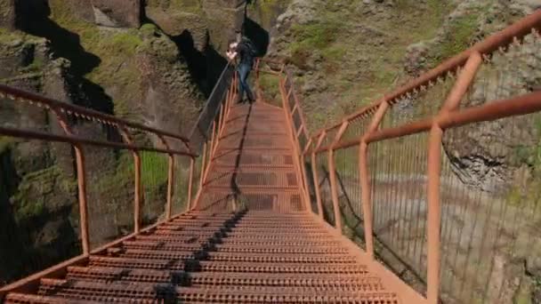 Young man taking photo of ravine on mobile. Fly over steel lookout platform high above deep rocky gorge. Fjadrargljufur canyon, Iceland — Stock Video