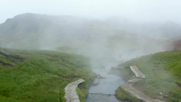 Les gens se baignent dans la rivière thermale dans la nature. En avant voler au-dessus de l'attraction touristique avec promenade le long de l'eau. Islande — Video