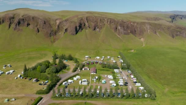 Yüksek kayalıkların altındaki kamp alanının hava görüntüleri. Güneşli bir günde kadife ve kervanın kaydırak ve tava fotoğrafını çek. İzlanda — Stok video
