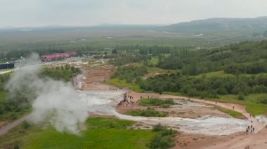 İnsanlar ayakta durup Geysir 'in kaynar su püskürmesini izliyor. Doğadaki jeotermal aktivitenin kayma ve pan görüntüsü. İzlanda