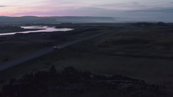 ภาพทางอากาศของรถขับบนถนนในชนบท พื้นผิวน้ําสะท้อนท้องฟ้ามืดที่มีสีสัน การติดตามรถ ไอซ์แลนด์ — วีดีโอสต็อก