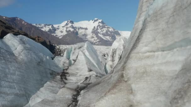 転送大小の谷の氷河の氷のブロックの間の隙間に飛ぶ。背景に青空に対する雪の山のピーク。アイスランド — ストック動画