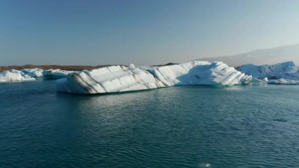 Diapositiva y panorámica vista en ángulo bajo de fragmentos del glaciar flotando en el lago ártico. Bloques de hielo al atardecer. Islandia — Vídeo de stock
