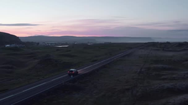 Spårning av bilkörning på väg på landsbygden. Silhuett av bergskammen mot färgglada skymning himmel i bakgrunden. Island — Stockvideo