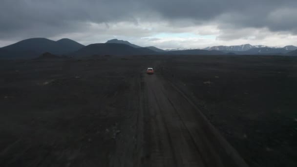 Voorwaarts volgen van auto op onverharde weg in dor landschap. Noordse vlaktes en bergkammen op de achtergrond. IJsland — Stockvideo