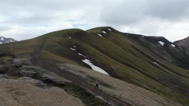 A respirar imagens de um jovem a subir a colina no caminho certo. Orbit tiro ao redor desportista na bela paisagem nórdica com lagos e montanhas. Islândia — Vídeo de Stock