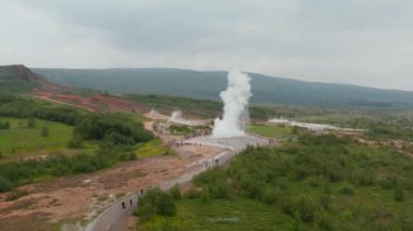 Jeotermal sıcak kaynak kaynayan su ve buhar bulutu fışkırıyor. İnsanlar Geysir aktivitesini yakından izliyor. İzlanda