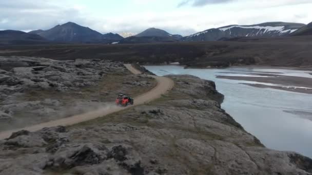 Flygbilder på offroadbilar som kör på grusväg längs sjön. Nordiskt vulkanlandskap. Mörka moln på himlen. Island — Stockvideo