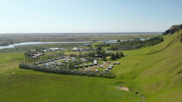 Vuela por encima del camping en el campo. Chalets y caravanas en zona bordeada de árboles. Río y pueblo en el fondo. Islandia — Vídeos de Stock