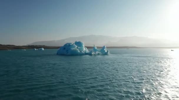 Gran bloque de hielo azul flotando en la superficie del lago iluminado por el sol brillante. Derretimiento del glaciar nórdico. Islandia — Vídeos de Stock