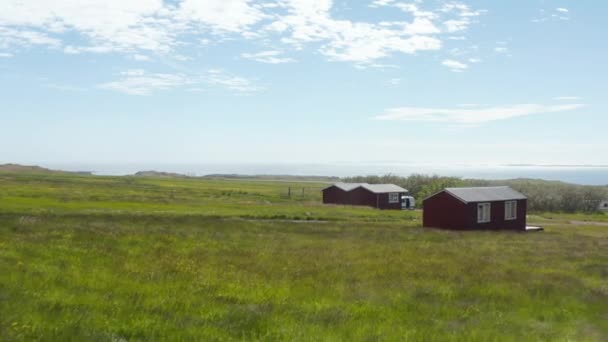 Μπροστά πετούν γύρω από ξύλινα σαλέ σε βοσκοτόπια τακτοποιημένη ακτή της θάλασσας. Αέρας κινείται λεπίδες του χόρτου. Ισλανδία — Αρχείο Βίντεο