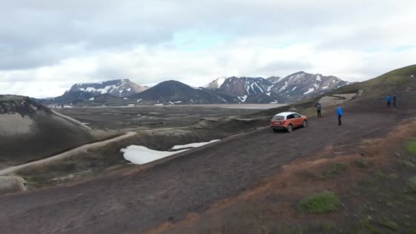 Пролететь над группой людей, стоящих вокруг автомобиля на возвышенной грунтовой дороге. Удивительная скандинавская панорама. Исландия — стоковое видео