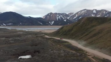 Güzel İskandinav manzarasının inanılmaz panoramik görüntüleri. Toprak yolda arabanın izini sürüyorum. Yamaçlarda kar kalıntıları olan bir dağ sırtı. İzlanda