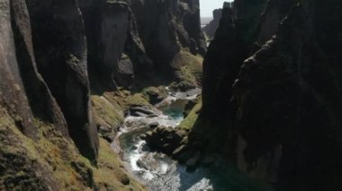 İleriye doğru uçurumun dibindeki derenin üzerinden uçar. Dik kaya duvarları ve suyun etrafındaki yeşil bitki örtüsü. Fjadrargljufur Kanyonu, İzlanda