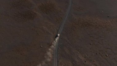 Volkanik arazideki tozlu toprak yolda hızlı giden arabanın yüksek açılı görüntüleri. Yükselen toz bulutları. İzlanda