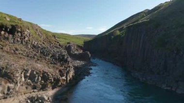Düzenli bazalt sütunlardan oluşan duvarlarla kanyon boyunca uçuyor. İnsanlar doğal cazibeyi görüyor. Studlagil Kanyonu, İzlanda