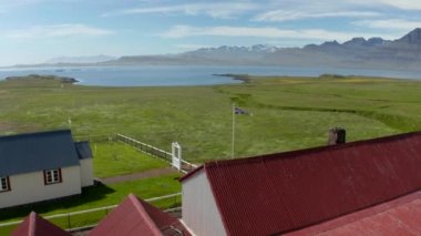 İzlanda ulusal bayrağı bina ve şapelin önünde direkte. Rüzgarda dalgalanan bayrak etrafında yörünge atışı. İzlanda