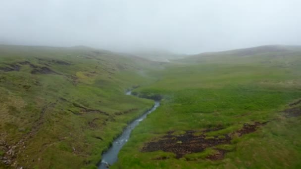 Előre repül a patak felett kanyargó füves területen. Termálvíz folyik le. Ködös idő van vidéken. Izland — Stock videók