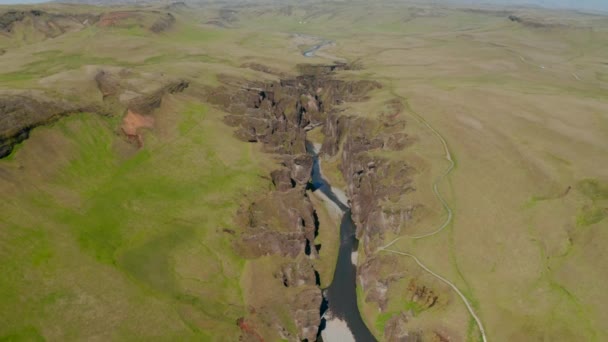 Foto aérea de arroyo que fluye desde el barranco con paredes rocosas rugosas. Revelar hacia atrás de la carretera y estacionamiento. Cañón de Fjadrargljufur, Islandia — Vídeos de Stock