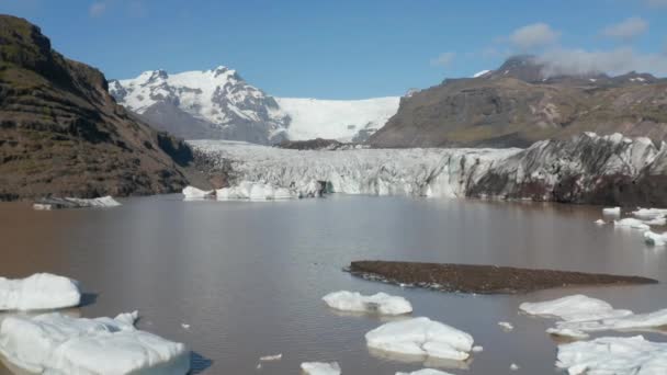 Flyg över vattenytan vid glaciärens slut. En ström av is som leder i dalen. Snöig fjällås i bakgrunden. Island — Stockvideo