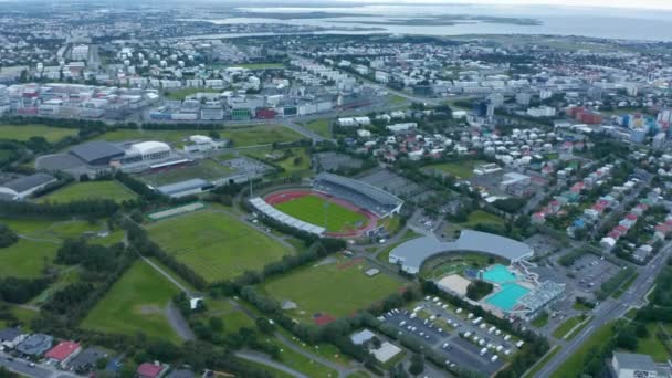 Aerial footage of football fields and swimming pools. Tilt up reveal of city and sea. Overcast sky. — Stock Video