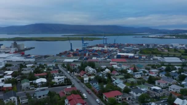 Vorwärts fliegen über Einfamilienhäuser in urbaner Nachbarschaft. Stapel von Marinecontainern und riesigen Kränen im Hafen. — Stockvideo