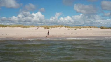 İnsanlar kumsalda güneşli bir günün tadını çıkarıyorlar. Sporcu hafif dalgalarla kıyıları yıkıyor. Yaz tatilinde. Danimarka