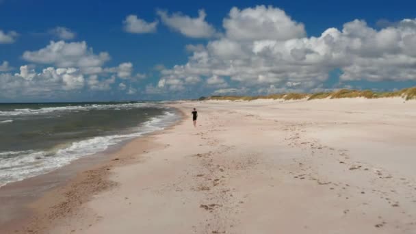 Śledzenie wstecz osoby biegnącej wzdłuż północnego wybrzeża morza. Boso-nożny sportowiec cieszący się miękkim piaskiem na plaży. Dania — Wideo stockowe