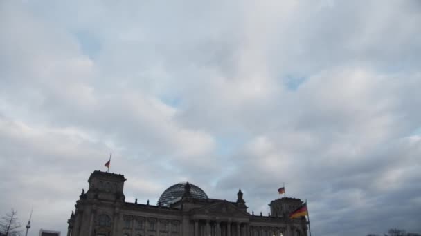 Хмарове небо, нахил вниз розкриває історичну і знамениту будівлю німецького парламенту. Національні прапори махають на полюсах. Берлін (Німеччина) — стокове відео