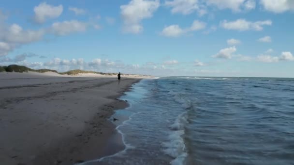 Leť nad vlnami omývajícími mořské pobřeží. Projíždí kolem sportovce běžícího na písečné pláži. Místo letních prázdnin. Dánsko — Stock video