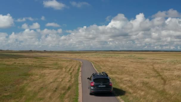 Carro dirigindo no estreito asfalto estrada sinuosa no campo plano. Vastas pastagens costeiras no dia ensolarado. Dinamarca — Vídeo de Stock