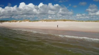 Kıyı manzarasının panorama eğrisi görüntüsü. Güneşli bir günde deniz kıyısında kumsalda koşan bir adam. Danimarka