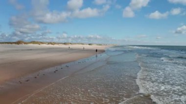 İnsanlar kumsalda rüzgarlı bir günün tadını çıkarıyor. Kumlu sahilde uçurtma uçurmak ya da koşmak. Denizden gelen küçük dalgalar. Danimarka
