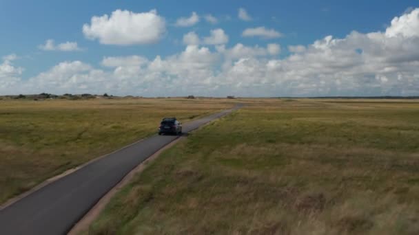 Kırsal bölgedeki asfalt yolda araç takibi. Düz çimen manzarası ve bulutlu mavi gökyüzü. Danimarka — Stok video