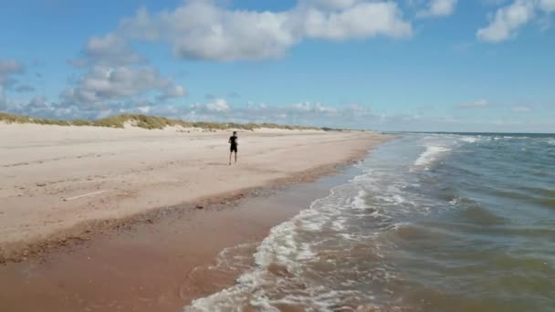 Sledování aktivní osoby na pláži. Běžící po písku podél vln omývajících pobřeží. Místo letních prázdnin. Dánsko — Stock video