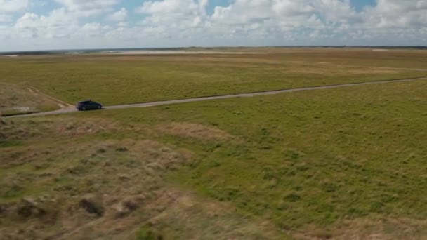 Letecký záběr auta jedoucího po úzké silnici na venkově. Ploché travnaté porosty a les v dálce. Dánsko — Stock video