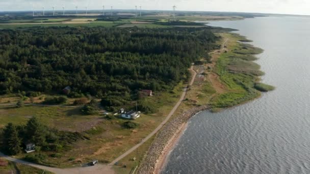 Aerial shot of sea coast. Cottages at forest and walkway along shore. Wind park providing green sustainable energy in background. Denmark — Stock Video