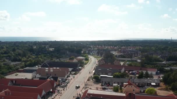 Achterwaartse vliegstraat in Oksby. Uitzicht vanuit de lucht op grote gebouwen langs de weg, winkels en diensten in een klein stadje aan de zeekust. Zomer vakantiebestemming. Denemarken — Stockvideo