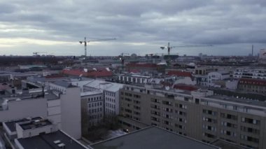 Şehir çevresindeki binaların üzerinden ileriye doğru uçuyor. Bulutlu gökyüzüne karşı bir grup vinç. Berlin, Almanya