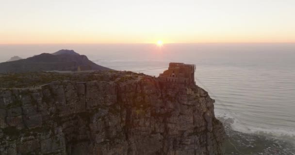 Luftaufnahmen vom Tafelberg-Flachgipfel mit Bergstation der Seilbahn. Fliegen Sie bei Sonnenuntergang um einen hohen Felsen über der Meeresküste. Kapstadt, Südafrika — Stockvideo