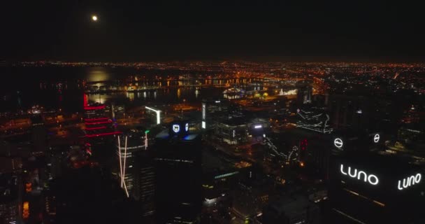 Geceleri limanı olan yüksek deniz manzaralı bir yer. Şehir merkezindeki yüksek katlı ofis binalarının tersten görünümü. Ay ışığı su yüzeyine yansıyor. Cape Town, Güney Afrika — Stok video