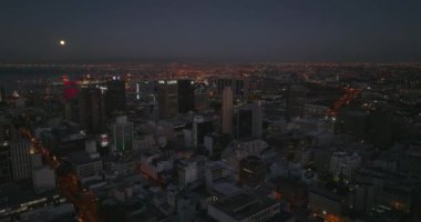 Gece şehir merkezindeki yüksek binaların panoramik görüntüsü yükseliyor. Arka planda liman var. Cape Town, Güney Afrika