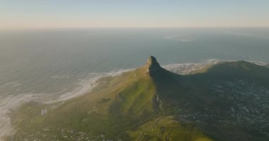 Okyanus kıyısının hava görüntüleri. Şehir semtlerindeki evlerin tepelerinde yükselen sivri bir dağ. Cape Town, Güney Afrika