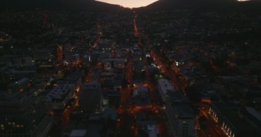 Gece görüş açısı, gece kasabasındaki aydınlık sokakları gösteriyor. Alacakaranlık gökyüzüne karşı dağ siluetlerini göster. Cape Town, Güney Afrika