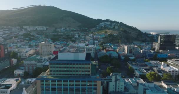Flyg över höga byggnader och på väg mot bostadsområdet Bo Kaap. Rader av färgade låga hus och träd på toppen av Signal Hill i bakgrunden. Kapstaden, Sydafrika — Stockvideo