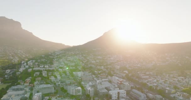 Vpřed, klesající létat nad budovami v městské čtvrti. Pohled proti jasnému slunci, postupné skrývání záře za vrcholkem hory. Kapské Město, Jihoafrická republika — Stock video