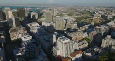 Şehir merkezindeki yüksek binaların üzerinden uç. Şehirde güneşli bir gün. Deniz koyunda mavi suyu olan panoramik görüntüler. Cape Town, Güney Afrika