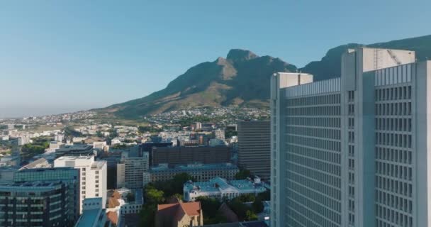 Voorwaarts vliegen langs hoog gebouw in de stad. Verhoogde beelden van stadsdeel en bergen op de achtergrond. Kaapstad, Zuid-Afrika — Stockvideo