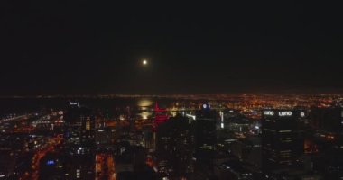 Şehrin merkezindeki gecenin hava indirme görüntüleri. Deniz koyundaki uzun iş binaları ve su yüzeyi ay ışığını yansıtıyor. Cape Town, Güney Afrika
