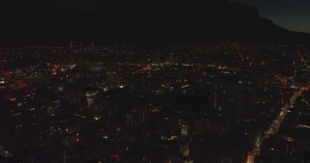Leć nad nocnym miastem. Świecące światła uliczne w miejskiej dzielnicy. Sylwetka gór w tle. Kapsztad, Republika Południowej Afryki — Wideo stockowe